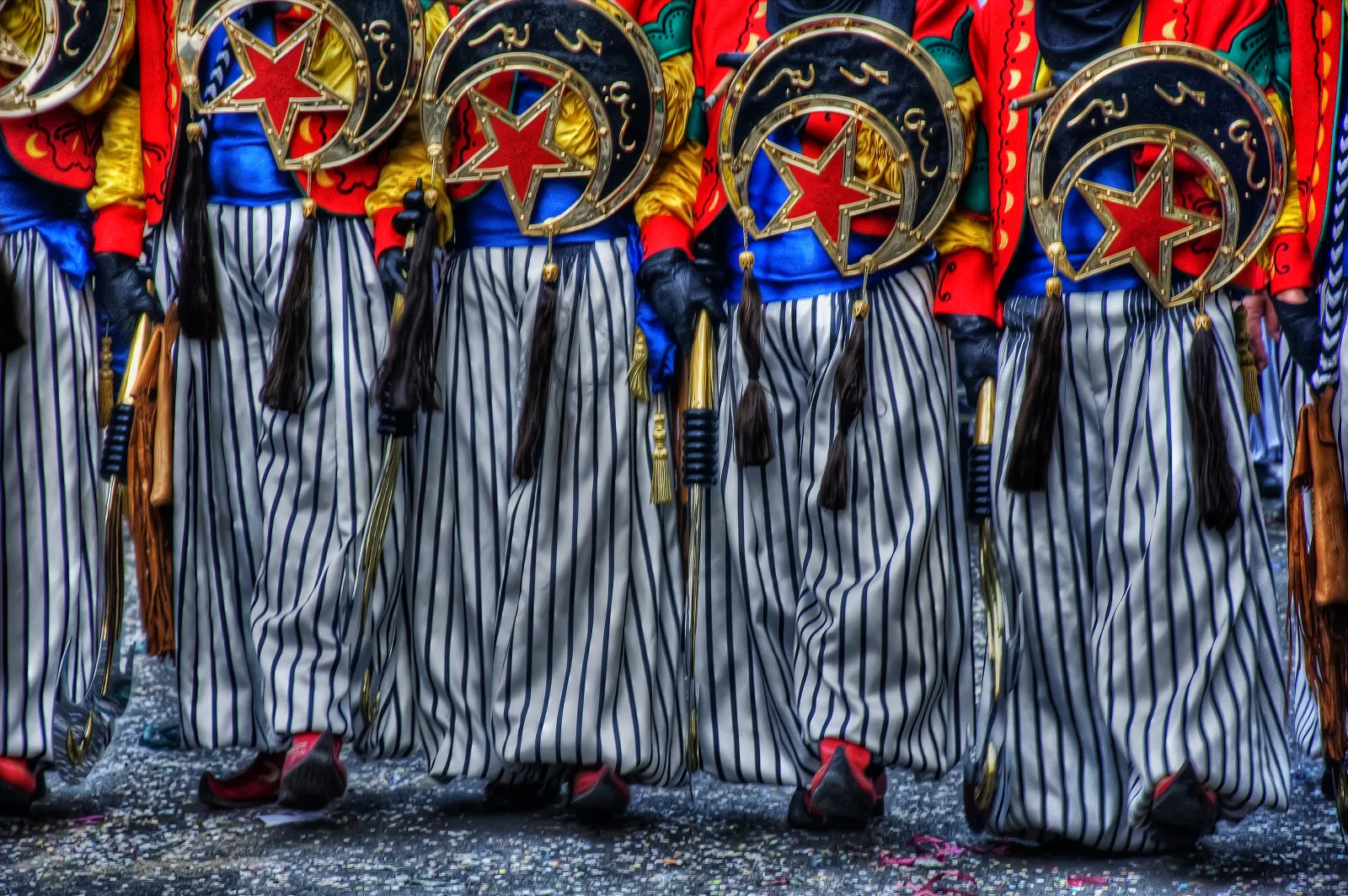 Indumentaria festera de colores vivos y pantalones a rayas durante un desfile de Alcoy