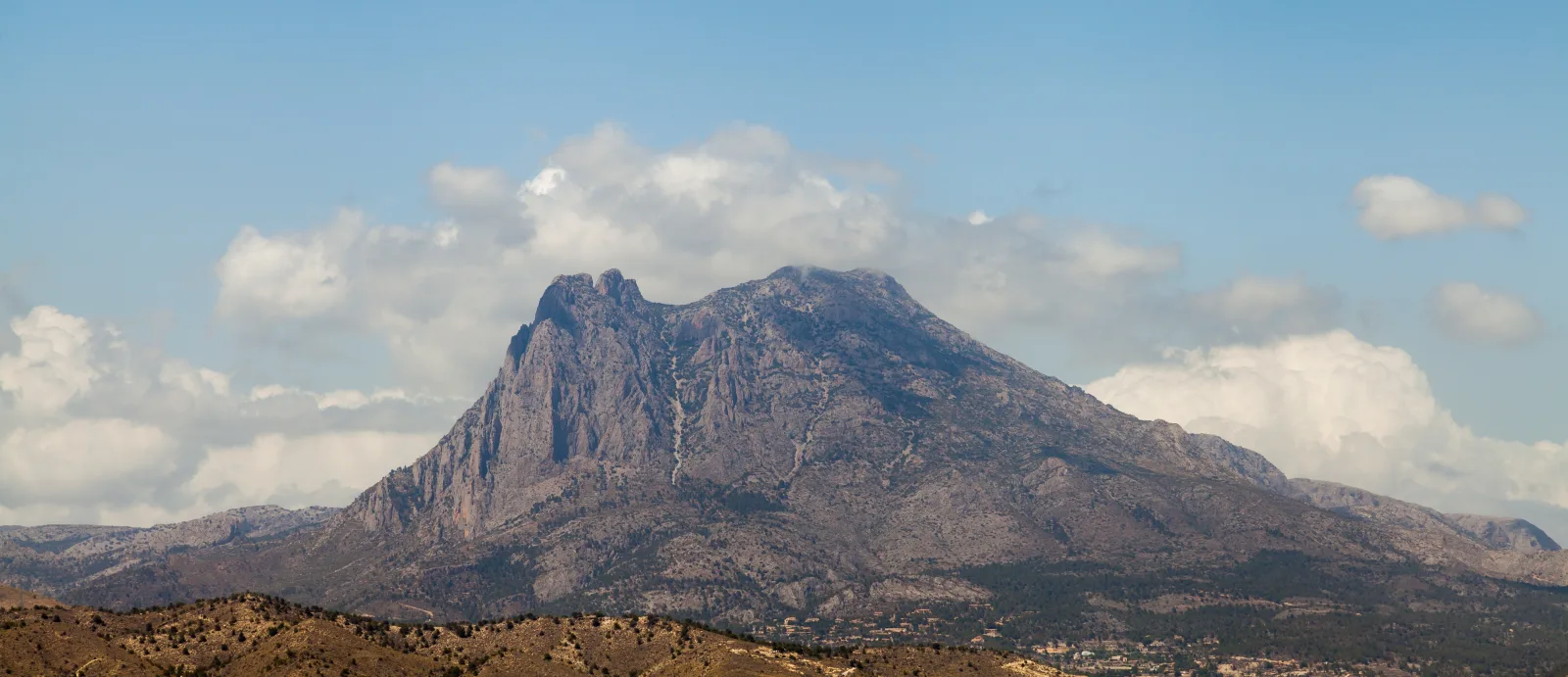 Silueta rocosa del Puig Campana con su característica hendidura bajo un cielo con nubes