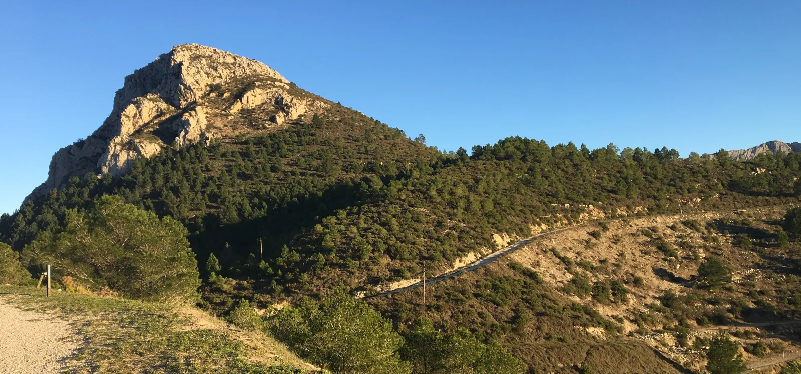 Ladera boscosa y relieve de roca caliza en el entorno de Coll de Rates bajo un cielo azul