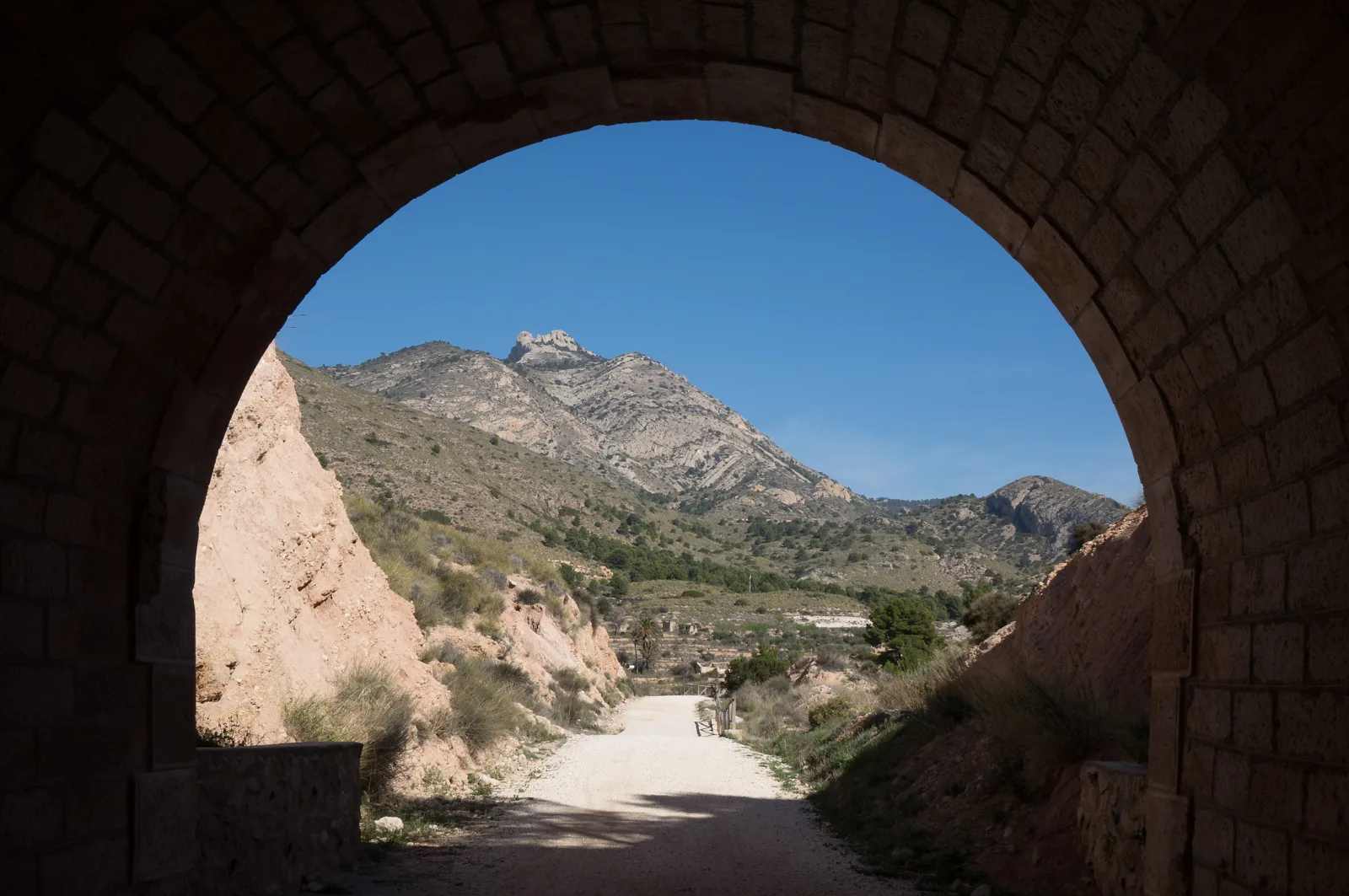 Camino de la Vía Verde del Maigmó y montañas vistos a través de un arco de túnel