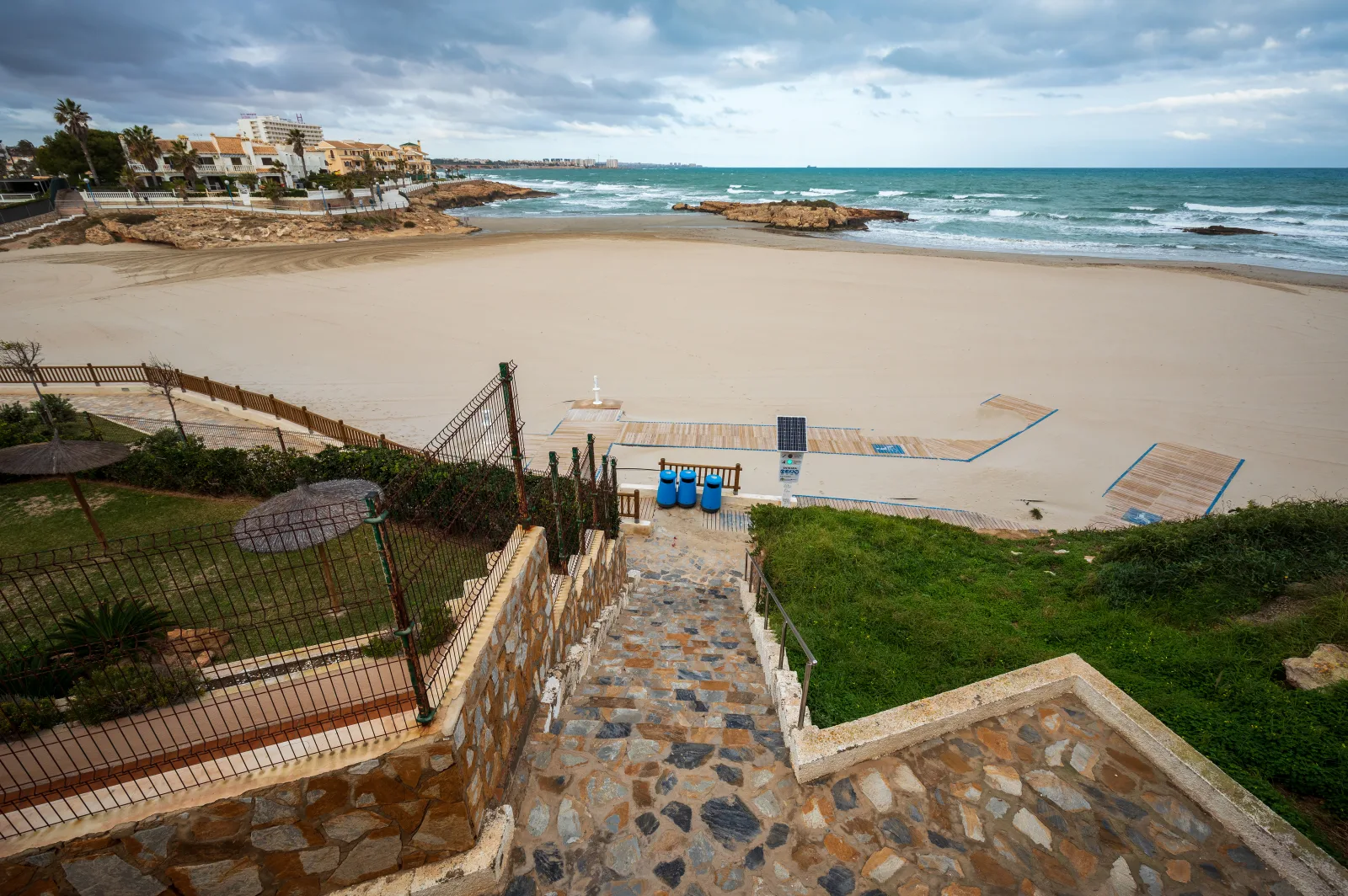 Playa de arena de Cala Capitán con escaleras de acceso, costa rocosa y olas